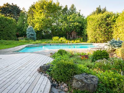 Backyard rock garden with outdoor inground residential swimming pool, curved wooden deck and stone patio
